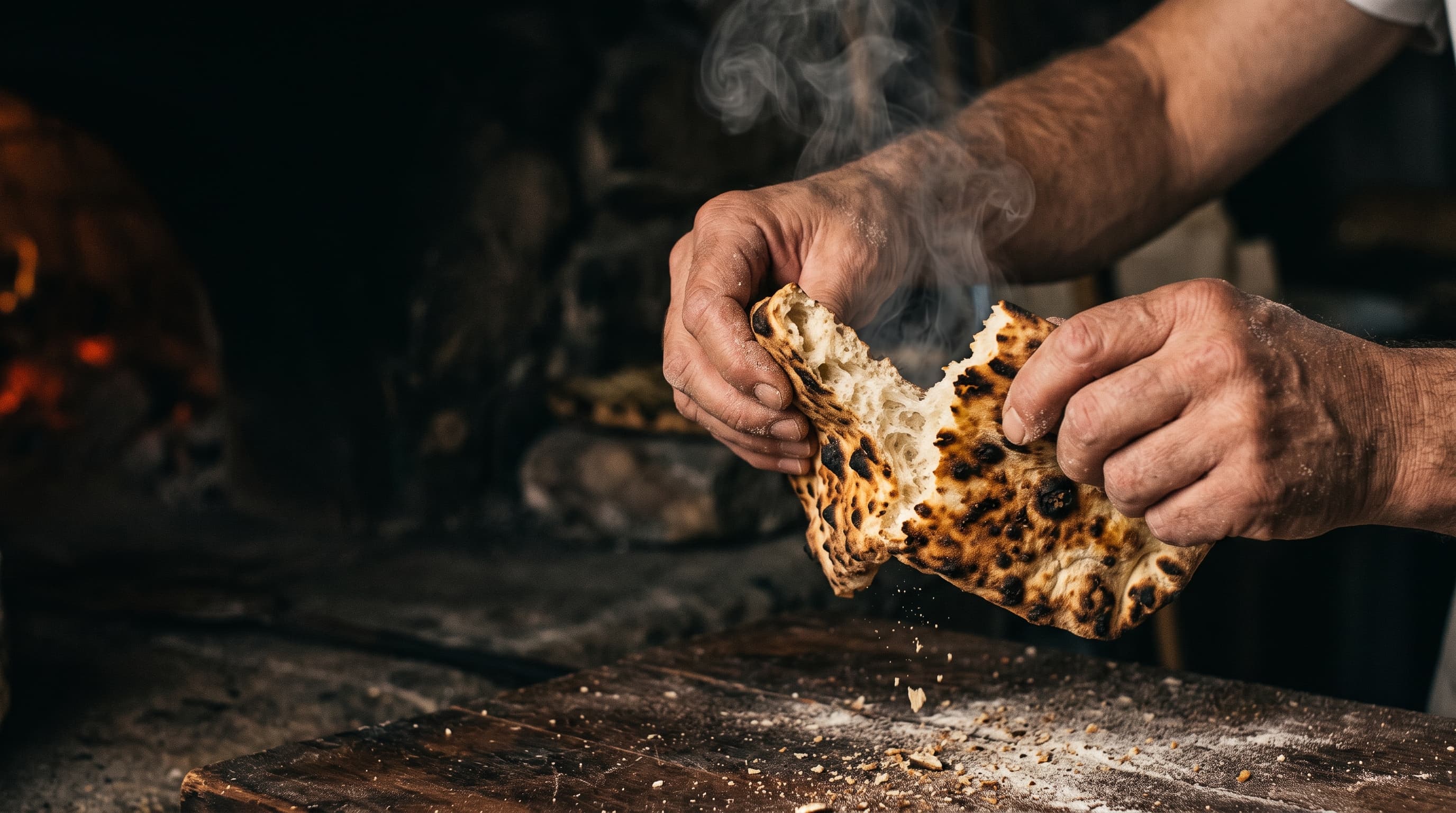 Hands tearing hot bread fresh from the oak oven, steam rising